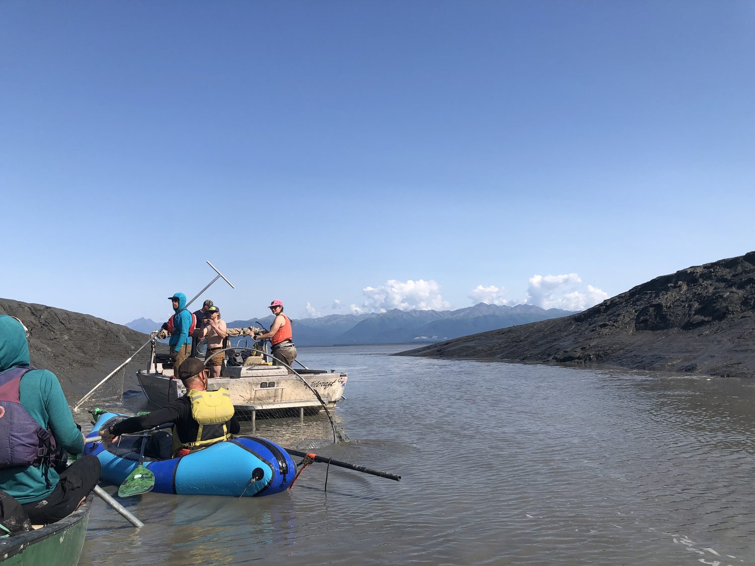 Packrafts and a skiff on a silty river with dip nets