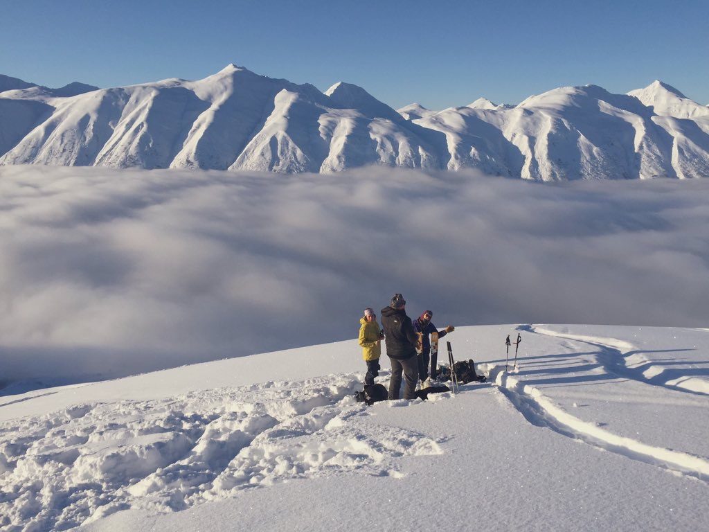 Ski touring on a ridge above a cloud inversion, snow-covered peaks behind